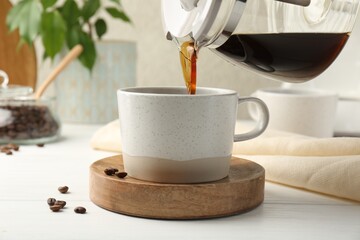 Pouring coffee into cup at white wooden table, closeup