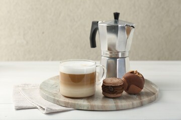 Aromatic coffee in cup, tasty macarons and moka pot on white wooden table