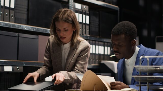 Policewoman with rucksack enters office with african american investigator clutching case papers. While female detective sets laptop on desk, policeman talks about the evidence and suspect profile.