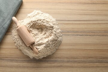 Pile of flour and rolling pin on wooden table, top view. Space for text