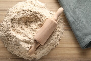 Pile of flour and rolling pin on wooden table, top view