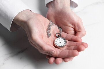 Man holding chain with elegant pocket watch at white marble table, closeup
