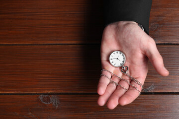 Man holding chain with elegant pocket watch at wooden table, top view. Space for text