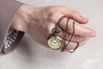 Man holding chain with elegant pocket watch at light marble table, closeup