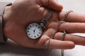 Man holding chain with elegant pocket watch at light textured table, closeup