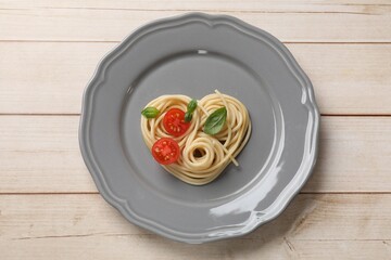 Heart made of tasty spaghetti, tomato and basil on wooden table, top view