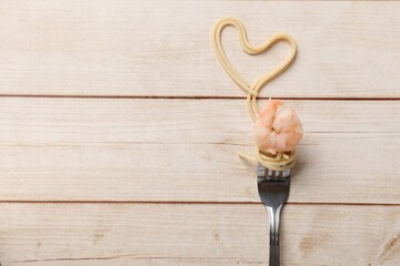 Heart made of tasty spaghetti, fork and shrimp on wooden table, top view. Space for text