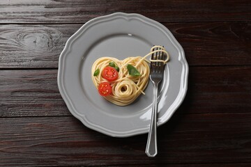 Heart made of tasty spaghetti, fork, tomato and basil on wooden table, top view