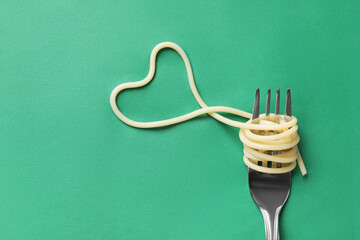 Heart made of tasty spaghetti and fork on green background, top view