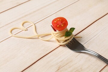 Heart made of tasty spaghetti, fork, tomato and basil on wooden table, closeup