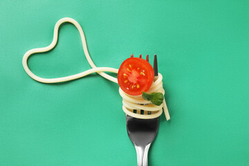 Heart made of tasty spaghetti, fork, tomato and basil on green background, top view