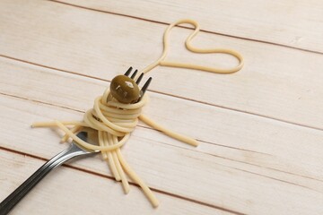 Heart made of tasty spaghetti, fork and olive on light wooden table. Space for text