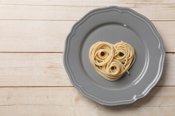 Heart made of tasty spaghetti on wooden table, top view. Space for text