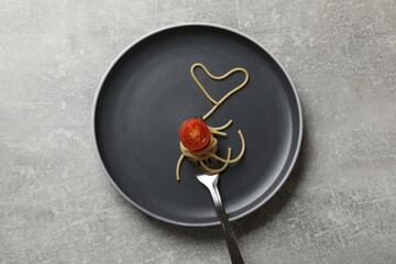 Heart made of tasty spaghetti, fork and tomato on light grey table, top view