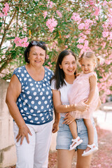 Laughing granny stands next to mom with a little girl in her arms in the garden