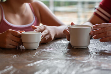 detailed shot of the hands of two girls holding a cup of tea or coffee in their hands