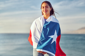 portrait beautiful latin woman holding over the shoulders a flag of Chile outdoors against blue sky, celebration and patriotism concept	