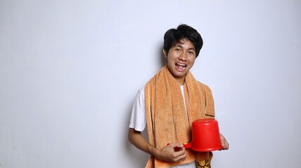 young Asian man wearing a white shirt, towel and holding a ladle to prepare to take a shower with...