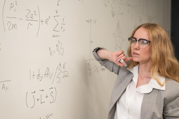 Young woman scientist writes formulas on a white board. 