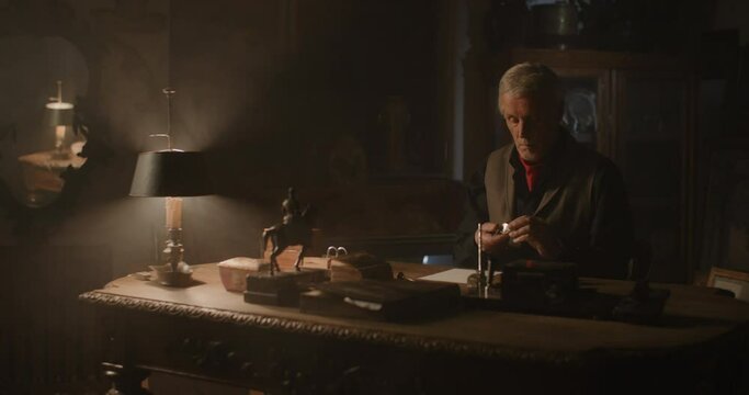 Old antique dealer evaluating objects at his desk.