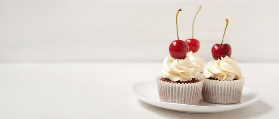Plate with tasty cherry cupcakes on table