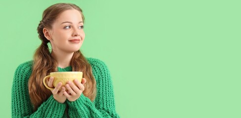 Beautiful happy young woman in warm sweater holding cup of hot tea on green background with space for text