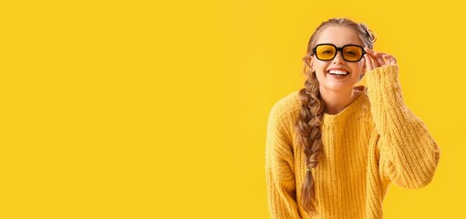 Beautiful happy young woman in warm sweater on yellow background with space for text