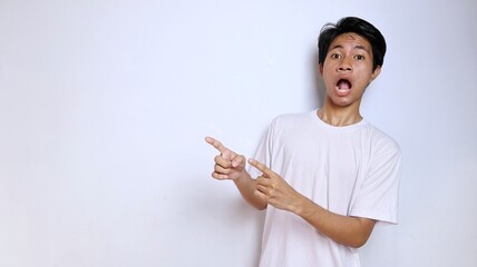 Excited young Asian man in white shirt with funny expression gesture pointing to the side