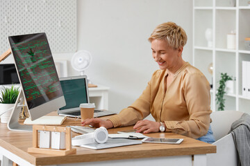 Mature female programmer working with computer at table in office