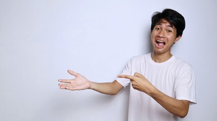 Excited young Asian man in white shirt with funny expression gesture pointing to open palm