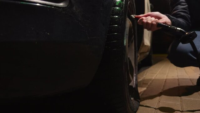 A man checks car flat tire pressure and pumps it up at night at a gas station