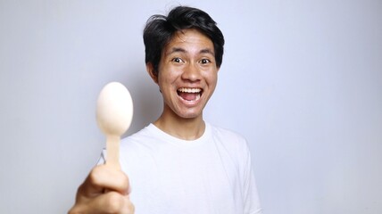 excited young asian man in white shirt gestures holding a spoon made of bamboo
