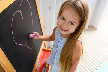 Cute little girl drawing on chalkboard at home, closeup