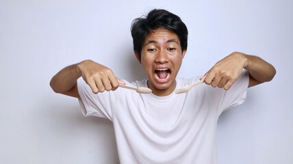 Excited young Asian man in white shirt gestures while eating holding spoon and fork made of bamboo