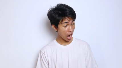 Young Asian man in white shirt with funny shocked gesture looking down