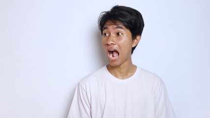 Young Asian man in white shirt with funny shocked gesture looking to the side