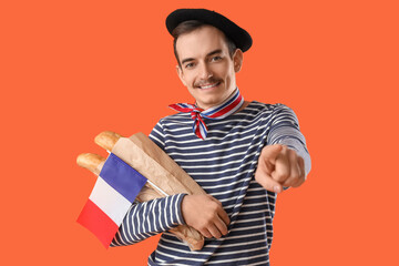 Handsome man with flag of France and baguettes pointing at viewer on orange background