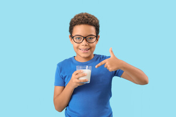 Little African-American boy pointing at glass of milk on blue background