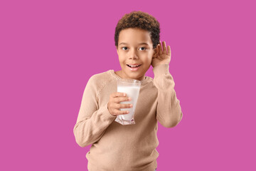 Little African-American boy with glass of milk hearing something on purple background