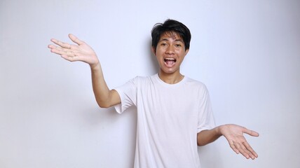 Excited young Asian man in white shirt gestures with open arms