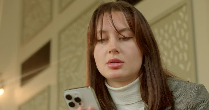 Young woman's face lights up with surprise as notification pops up on smartphone. Her curiosity is piqued, and she eagerly reaches for her phone to uncover the unexpected message.
