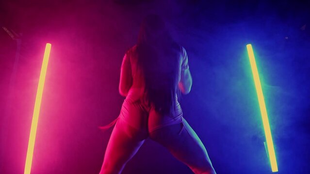Young seductive woman dancing, shaking, twerking buttocks, hips in multicolor light, studio background. Modern dance - twerk.