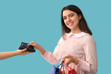 Young woman with credit card paying via payment terminal on blue background