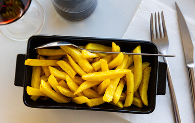 Table set for lunch there is black ceramic dish with portion of French fries. On light tablecloth...