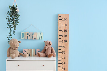 Wooden stadiometer and chest of drawers with plush toys near blue wall