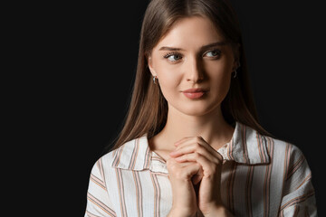 Young woman praying on black background, closeup
