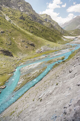 A blue mountain river flows in a mountain valley past green meadows, a mountain landscape with a...