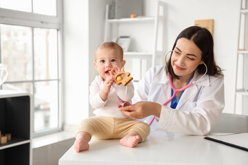 Female pediatrician listening little baby's lungs with stethoscope on table in clinic