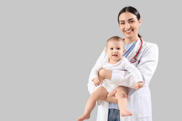 Female pediatrician with little baby on light background