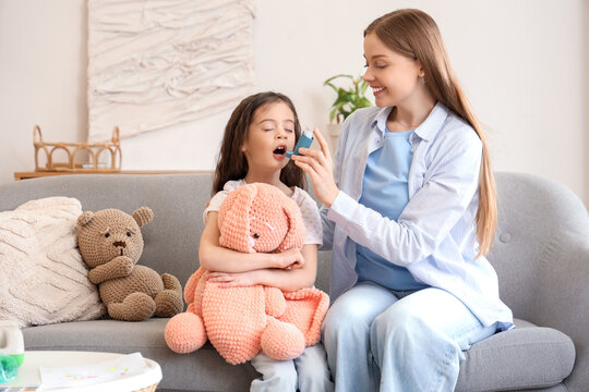 Little girl with her mother using inhaler at home